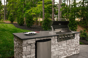 Modern Stainless Steel Grill Built Into a Stone Countertop with A Backyard Lawn