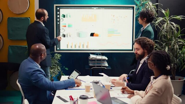 Project team reviewing monthly reports and data on interactive board, studying market trends and customer needs to ensure objectives fulfillment. Workers accomplish business goals. Camera B.