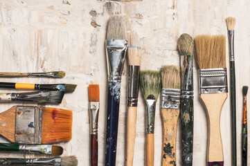 A row of vintage paint brushes on a beige primed canvas background. Artistic creativity concept.