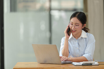 Asian businesswoman uses laptop and smartphone in open plan office business idea Data analysis,...