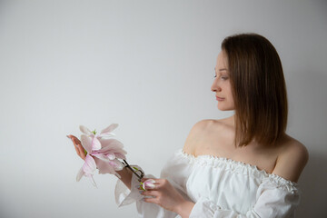 young elegant woman in white dress with spring flowers in vases on gray background - 782720109