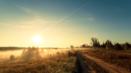 Rural landscape. Road to a field on a sunny foggy morning - 782724148