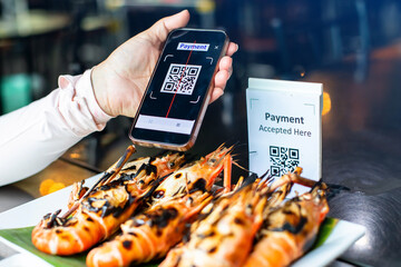 Selective focus to smartphone scan QR code payment tag with blurry grilled river prawns in...