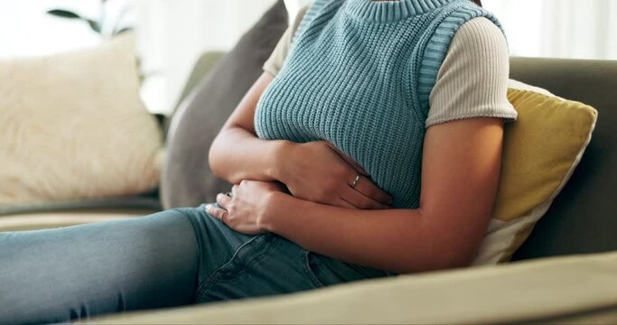 Woman, stomach and cramps pain in home for menstruation period, digestion or inflammation. Person, hands and bloated abdomen on sofa for uterus anatomy or stress anxiety for tummy ache, ulcer or hurt