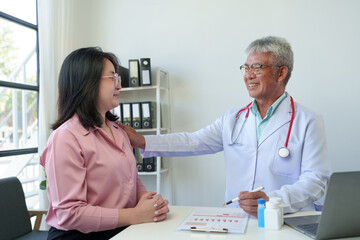 Fototapeta premium Asian elderly doctor with stethoscope holding female patient's shoulder Promote care, treatment, medication, therapy, and encouragement to fight. service concept Providing advice on life insurance.