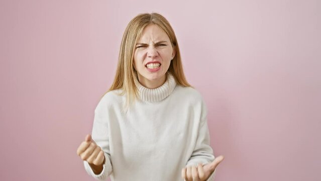 Furious blonde beauty, mad with rage, raises fist in anger - beautiful girl stands frustrated, shouting aggressively on pink isolated background