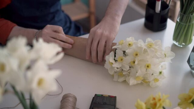 Male florist collecting a bouquet, close-up. Making a daffodils bouquet in a flower shop. Close-up of wrapping a bouquet in craft paper. Spring flowers