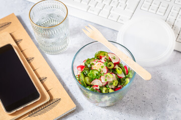 Healthy food in a office. Prepared radish and cucumber salad on  a desk with office supplies