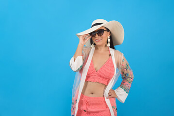 Woman wearing beach outfit and sunglasses with positive attitude. Studio portrait, blue background.
