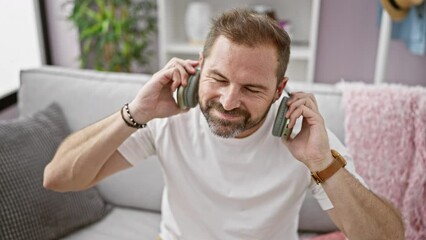 Mature man with headphones enjoying music on sofa indoors