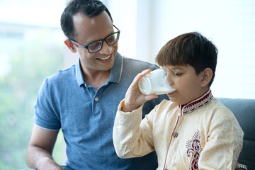 Indian father give boy glass of milk at home, Indian child wearing traditional clothes