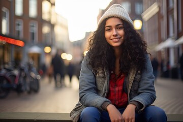 A woman with curly hair is sitting on a bench in a city street