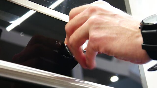 Close-up of a male hand pulling out the tuner knob of an electronic oven by pressing it and turning on the desired temperature of the oven