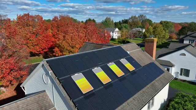Solar panels charging battery icons with animated energy generation effect. Roof with solar panels, autumn trees, and a clear blue sky. Aerial revealing American neighborhood on bright sunny fall day.