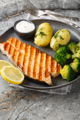 Close up of delicious grilled salmon with new potatoes, broccoli and cream sauce in a plate on the table. Vertical