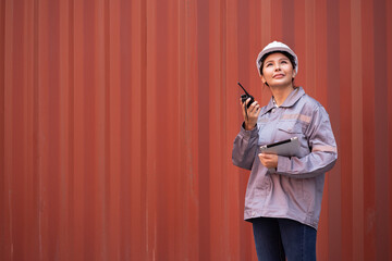 Portrait Asia logistic engineer woman worker or foreman working with tablet computer and walkie talkie at container site	
