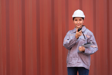 Portrait Asia logistic engineer woman worker or foreman working with tablet computer and walkie talkie at container site	