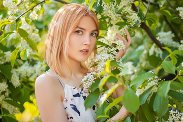 Close-up portrait of an attractive young woman dressed in a dress posing against a background of blooming white apple flowers.