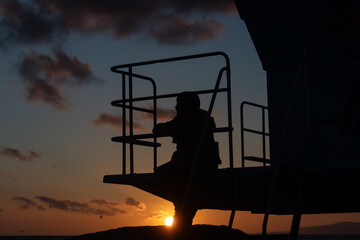 Extreme Closeup of Silhouette of Girl Sitting on Lifeguard Tower During Vivid Sunset Looking Toward...