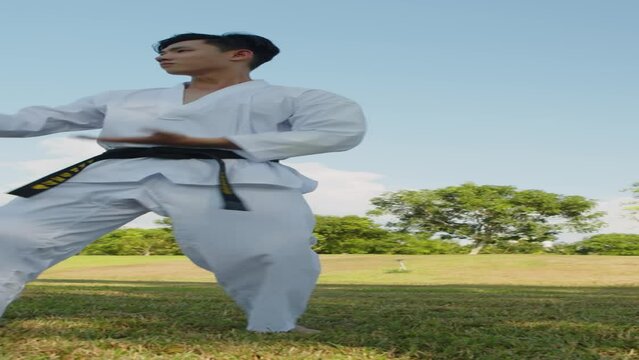 Vertical shot of Asian gen Z sportsman in dobok practicing taekwondo stances outdoors alone