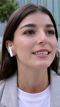 Vertical 9:16 video. Young business woman talking on the cellphone using wireless earphones while sitting at outdoor area of office building center. Technology and business concept.
