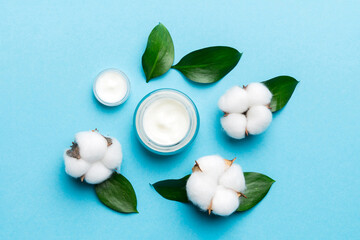 Organic cosmetic products with cotton flower and green leaves on color background. Flat lay