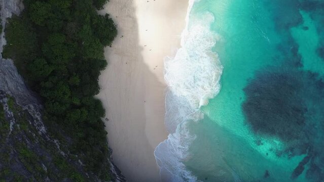 Drone shot top view of waves breaking on a white sand beach in Bali. Clear turquoise water in tourist destination
