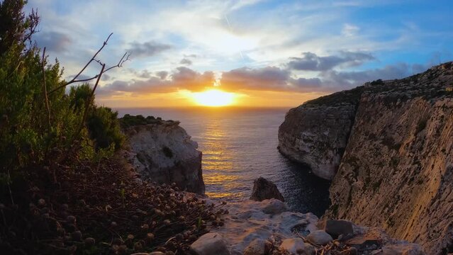 Golden sunset captured in a time-lapse, descending over serene rocky cliffs by the sea.