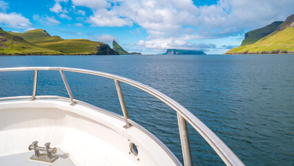 View of the tourist boat cruising at Faroe Islands fjords at blue sky and sunny day.