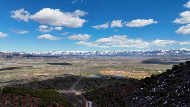 Aerial-View of farms and valley fields with distant snowy mountain-Pull back into narrow rocky canyon with small patches of snow on the shady side.