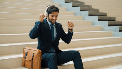 Professional business man picking and listening music by using headphone while sitting at stairs....