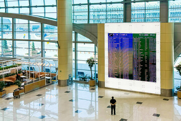 lone traveler stands in a spacious, modern airport, attentively checking the flight information...