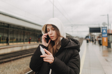 Tourist teenage girl at train station using smartphone map, social media check-in, or buy ticket booking. Modern travel app technology, lone traveler, Winter vacation railroad adventure concept - 782858556