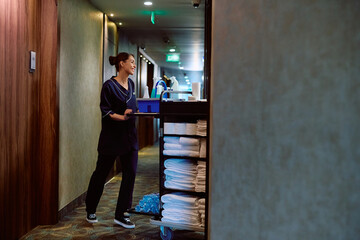 Happy housekeeper pushing chambermaid's trolley while cleaning guest rooms in  hotel.