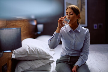 Young businesswoman having  glass of water while relaxing in hotel room.