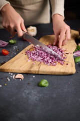 Woman chopping red Mars onion on wooden cutting board at domestic kitchen