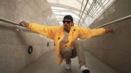 Skilled happy asian hipster walking while dancing in narrow corridor. Close up of break dancer...