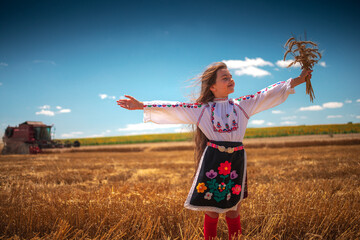 Bulgarian girl clothing folklore embroidery costume in agricultural wheat field during harvest and combine machine - 782872740