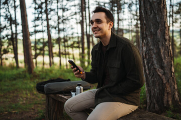 Obraz premium One caucasian male taking a break while hiking on the bench while using mobile phone