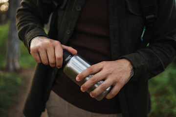 Close up of caucasian male hands opening metal water bottle while hiking