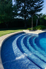Vertical view of a swimming pool in a private garden with jets pumping water on a sunny summer day....
