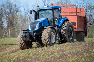 Closeup of blue farm tractor with fertilizer manure spreader on agricultural field with copy space