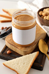 Peanut paste in a glass jar with a spoon, on a light background.