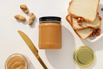  Peanut paste in a glass jar with a table knife, on a light background. © Atlas