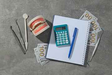 Jaw and dental instruments, calculator, cash and notepad on gray background, top view
