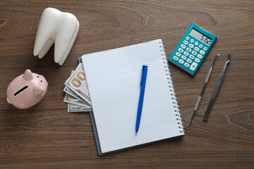 Tooth, dental instruments, piggy bank and cash, notepad and calculator on wooden background, top...