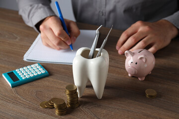 Tooth with dental instruments, piggy bank, calculator, coins and hands on table on gray background