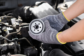 Auto mechanic holds fuel filter for diesel cars against backdrop of engine compartment, rotating it...