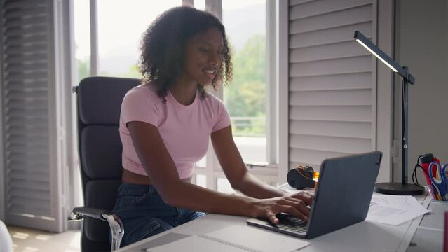 Teenage girl sitting at desk in bedroom at home doing homework on laptop - shot in slow motion