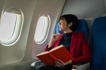 Smiling woman sitting by the airplane window, engrossed in writing notes in her orange notebook.